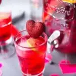 Clear glass of hibiscus punch with heart swizzle stick