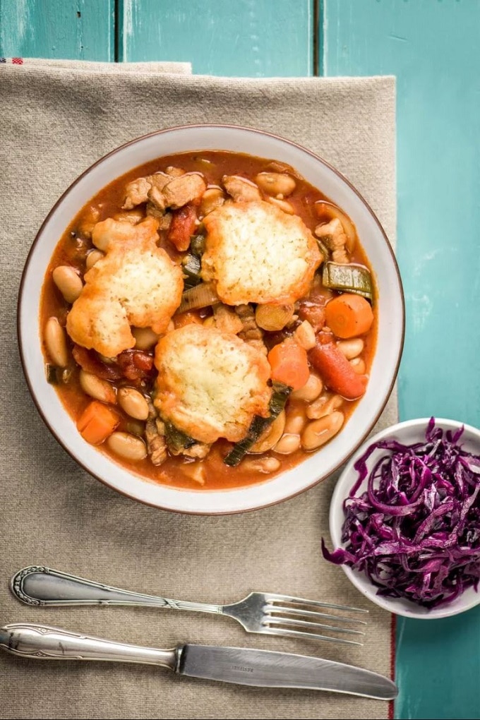 Bowl of pork belly casserole with dumplings and red cabbage with silverware