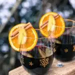 Two glasses of mulled wine with orange slices, ginger, and cinnamon