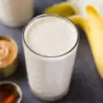 Peanut butter banana smoothie in a glass next to ingredients