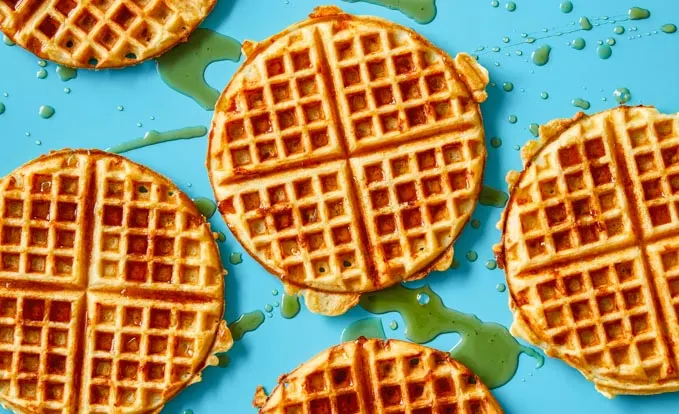 Cheddar waffles on a blue background with maple syrup dripped over them