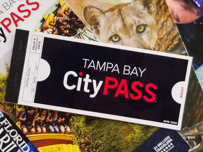 A Tampa Bay CityPASS paper voucher booklet on top of a ZooTampa guide and a Florida Aquarium guidemap