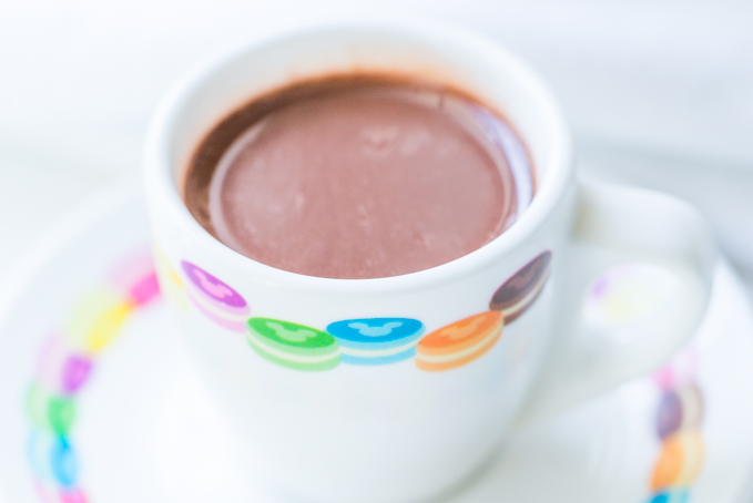 Closeup of hot chocolate in a white demitasse cup with rainbow macarons around the rim