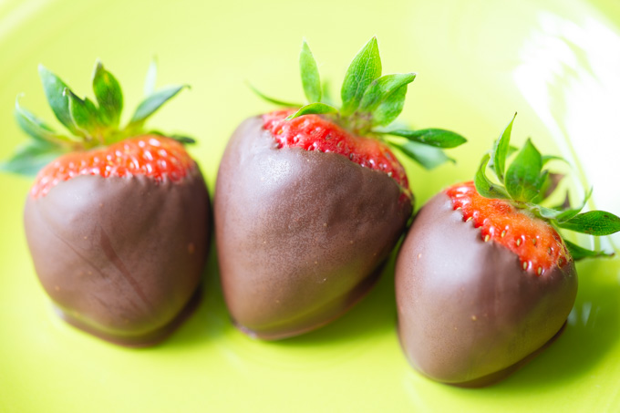 Three chocolate dipped strawberries on a green plate