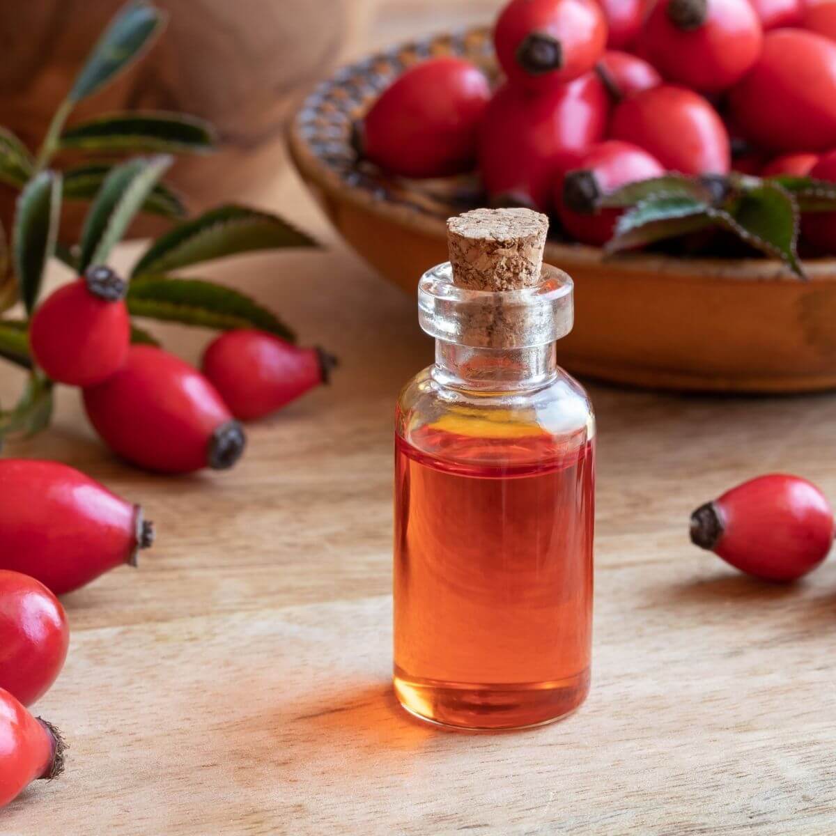 Clear glass bottle of rose hip seed oil with rose hips in the background, as used for minimalist skincare routine