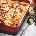 Baked macaroni and cheese in a red casserole dish next to a serving spoon
