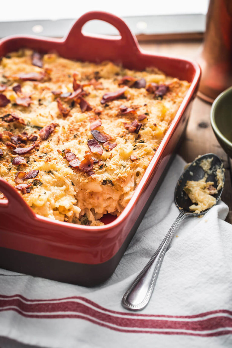 Baked macaroni and cheese in a red casserole dish next to a serving spoon