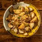 Lyonnaise potatoes in a rustic ceramic bowl on a wooden backdrop