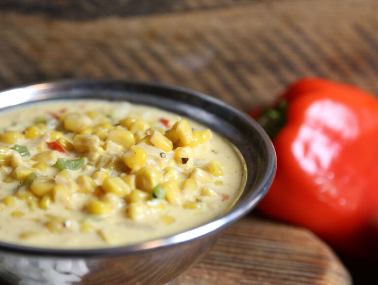 Metal bowl of maque choux corn side dish next to a red bell pepper